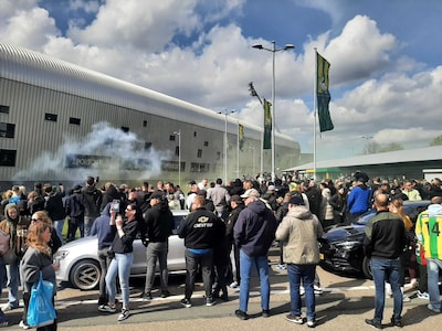 Grote groep supporters verzamelt zich bij stadion van ADO na kampioenschap, veel vuurwerk te horen