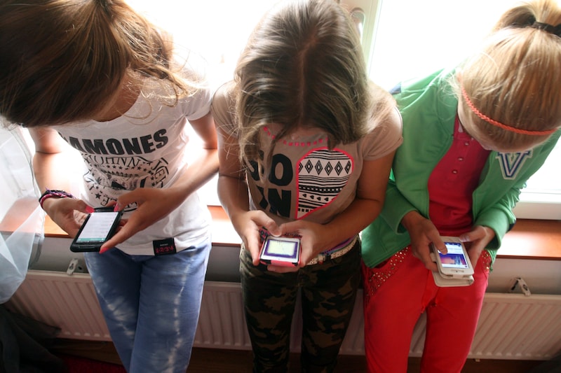 Jonge kinderen gaan gebukt over hun smartphone.