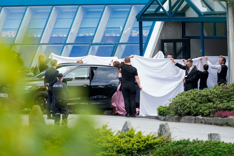 gasten-van-martha-louise-en-durek-worden-afgeschermd-met-grote-witte-doeken-terwijl-ze-naar-de-bruiloft-vertrekken