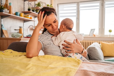 young-adult-mother-sitting-in-chair-at-home-holding-her-three-month-old-baby-son-feeling-tired-sleepy-or-having-a-headache